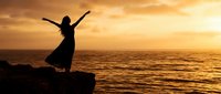 Woman silhouette with raised arms celebrating freedom on ocean cliff at golden sunset. Inspirational moment of joy and achievement by the sea.