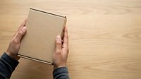 Caucasian male hands holding kraft cardboard box on wooden surface for shipping, delivery, and packaging concepts.