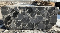 Natural stone slab with irregular black and gray marble pattern showing organic shapes and white veining, photographed outdoors in winter setting against snow.