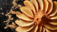 Orange flower petals arranged in circular pattern with scattered powder creating dramatic contrast against dark background, artistic food photography composition.
