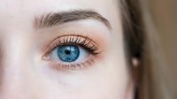 Close-up of young woman's blue eye with natural makeup and long eyelashes showing detailed iris patterns and healthy skin texture for beauty concepts.