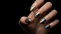 Stylish geometric nail art design with metallic gold silver and blue triangular patterns on manicured fingernails against dark background for beauty salon.