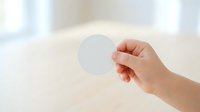 Hand holding blank white circle card against bright neutral background, suitable for mockups, branding presentations, and marketing materials.