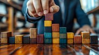 Business person arranging colorful wooden blocks in ascending pattern on wooden table, representing growth strategy and planning.