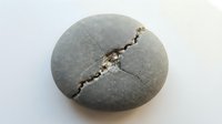 Close-up of a smooth gray stone with a natural crack running diagonally across its surface, showing mineral deposits within the fissure.