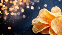 Crispy potato chips with salt on dark background with golden bokeh lights and sparkles creating festive atmosphere for food advertising and design.