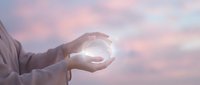 Hands cupped together holding glowing light orb against soft pink and purple sky background symbolizing hope, protection, and spiritual energy.