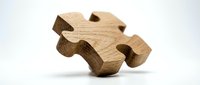 Wooden puzzle piece carved from natural oak wood with smooth edges and organic grain texture, isolated on white background for business solutions and teamwork concepts.