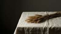 Wheat ears bundle on linen tablecloth creating rustic farmhouse atmosphere for harvest season decoration and natural organic food styling concepts.