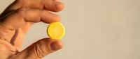 Hand holding fresh lemon slice against neutral background, suitable for food, beverage, health and wellness design projects.