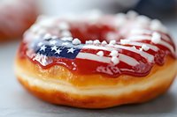Patriotic glazed donut with American flag frosting design featuring red white and blue icing on golden pastry for Fourth of July celebration dessert.