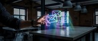 Hand holding holographic neon geometric shapes floating above table in modern loft workspace with brick walls and industrial lighting for technology and innovation concepts.