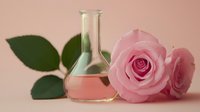 Rose essential oil in glass flask with pink roses and green leaves on pastel background, natural cosmetic ingredient concept.