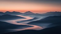 Misty mountain landscape at sunrise with layered peaks and valleys filled with morning fog creating ethereal atmosphere in soft pink and blue tones.