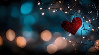 Red glitter heart decoration hanging on branch with fairy lights against blurred bokeh background in turquoise and warm tones creates romantic mood.