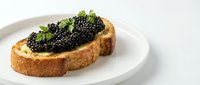 Toasted bread slice topped with creamy spread and luxurious black caviar served on white plate for gourmet appetizer or fine dining.