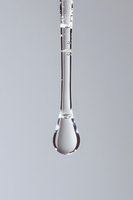 Single water drop suspended in mid-air with crystal clear transparency against light gray background, showcasing surface tension and liquid dynamics in macro photography.
