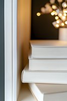Stack of white hardcover books on windowsill with soft bokeh lights in background creating cozy reading atmosphere. Minimalist composition for literature concept.