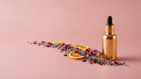 Golden dropper bottle with natural dried flowers and herbs on pink background for skincare cosmetics and aromatherapy products.
