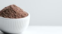 Finely ground cocoa powder in white ceramic ribbed bowl against light background. Natural raw cacao ingredient for baking and chocolate making.
