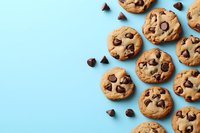Freshly baked chocolate chip cookies arranged on light blue background with scattered chocolate chips for baking and dessert concepts.