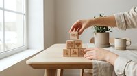 Woman hands arranging wooden blocks with heart and home symbols on table near window creating cozy domestic atmosphere for lifestyle concepts.