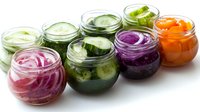 Colorful assortment of pickled vegetables in glass jars including red onion, cucumber, cabbage and carrot slices arranged in row on white background.