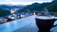 Morning coffee cup on balcony railing with blurred mountain landscape and city lights bokeh background, peaceful dawn atmosphere with hot beverage.