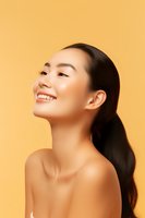 Young Asian woman with glowing skin and natural makeup smiling confidently against orange background, showcasing beauty and skincare concept.
