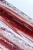 Macro photography of red crystalline structure with diagonal lines and sparkling water droplets creating abstract pattern with bokeh effect and light reflections.