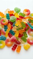 Colorful assorted gummy candies including bears, worms and rings scattered on white background. Sweet treats for confectionery and dessert concepts.