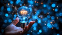 Glowing light bulb floating above palm against dark background with blue bokeh lights and magical sparkles, symbolizing innovation and creative ideas.