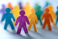 Colorful paper cutout figures standing together symbolizing diversity, inclusion and community. Purple figure in focus with blurred rainbow colored figures behind.