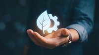 Businessman holding glowing leaf and gear icon, representing sustainable technology, green innovation, and eco-friendly business solutions for corporate growth.