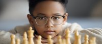 Young Asian boy wearing glasses contemplates chess strategy while leaning over game board with focused expression, representing education and strategic thinking.
