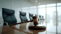 Wooden gavel and sound block on conference table in empty corporate boardroom with leather chairs, symbolizing legal proceedings or corporate governance.