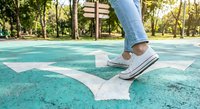 Person in white sneakers and jeans walking on turquoise arrow painted on asphalt path in sunny park. Concept of direction, progress, and moving forward.