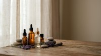 Amber glass bottles with essential oils and lavender flowers on wooden table near window with natural light for aromatherapy and wellness treatments.