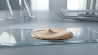 Young adult female with light skin tone applying creamy beige foundation or concealer on glass surface in bright, minimalist bathroom setting for cosmetics and skincare marketing.