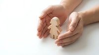 Protective hands cupping wooden child figure symbolizing care, safety, family protection and child welfare on white background.