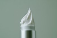 Cosmetic cream swirled on top of a silver tube against a soft green background, showcasing skincare product texture for beauty and wellness.