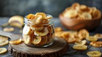 Healthy dried banana chips in glass jar on wooden board, perfect for natural snack food photography and healthy eating lifestyle concept. Dark rustic background.