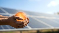 Hands holding glowing golden sphere with solar panels in background, representing renewable energy, sustainability, and clean power technology for eco-friendly solutions.