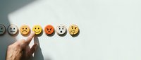 Young adult male hand selecting happy yellow smiley face emoji from row of emotion icons representing customer satisfaction, feedback, and service rating scale.