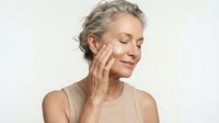 Mature Caucasian woman with gray curly hair gently touching face with closed eyes, skincare routine concept for anti-aging beauty and wellness products.