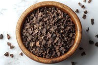 Dark chocolate chips scattered in wooden bowl on marble surface, with loose pieces around. Close up view of baking ingredients for cookies and desserts.