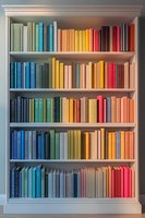 White bookshelf with colorful books arranged in rainbow spectrum order from blue and green to yellow, orange and red tones, creating vibrant home decor.