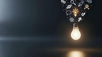 Glowing light bulb with innovation icons and gears floating above representing creative ideas, brainstorming, and business solutions on dark background.