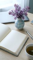 Cozy workspace with open notebook, lilac flowers in ceramic vase, tea cup, and pen on wooden desk for productivity and lifestyle concepts.