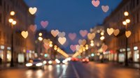 Romantic city street at night with glowing heart-shaped bokeh lights creating magical atmosphere for Valentine's Day celebration and love themes.